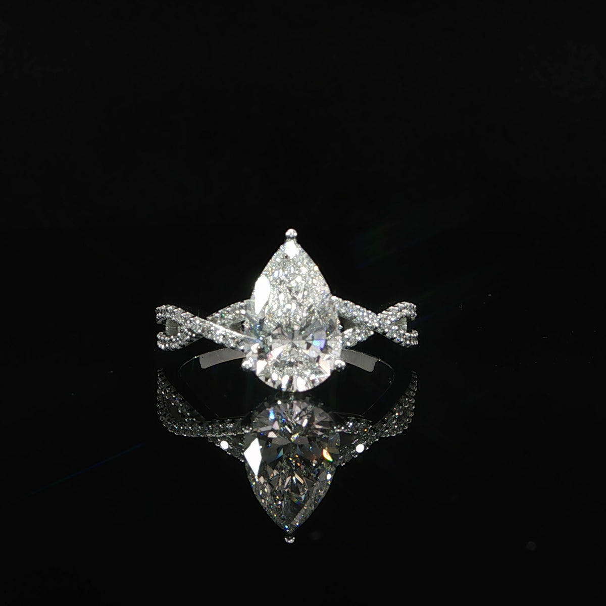 Front view of a pear-shaped diamond engagement ring featuring a hidden halo and twisting diamond band.