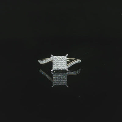Video of square diamond cluster and curved yellow gold shoulders reflected on a glossy black surface.