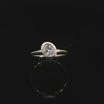 Video of an oval diamond framed by a smooth polished bezel setting in 14K yellow gold.