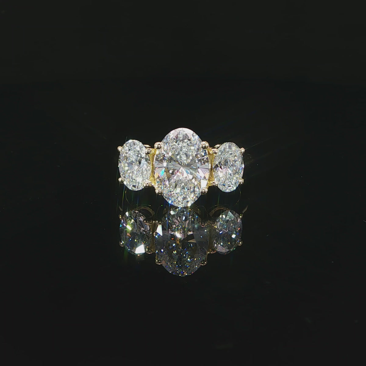 Centered front view of a yellow gold engagement ring with three vertically oriented oval diamonds.