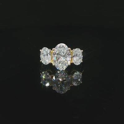 Centered front view of a yellow gold engagement ring with three vertically oriented oval diamonds.