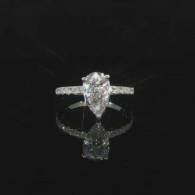 Video of a pear diamond ring with a pavé band mirrored on a glossy black surface.