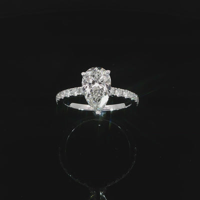 Front angle video of a white gold engagement ring with a pear center diamond and pavé-set shoulders.