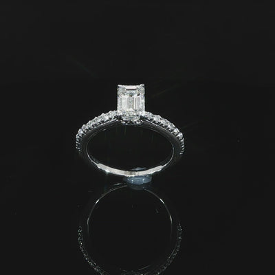 Angled emerald-cut solitaire with a diamond band, totaling 1.30 CTW, in 14K white gold against black.