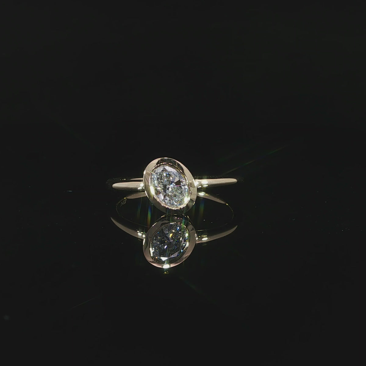 Close-up video of a modern oval bezel set engagement ring with a slim polished yellow gold shank.