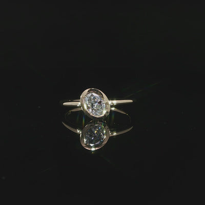 Close-up video of a modern oval bezel set engagement ring with a slim polished yellow gold shank.