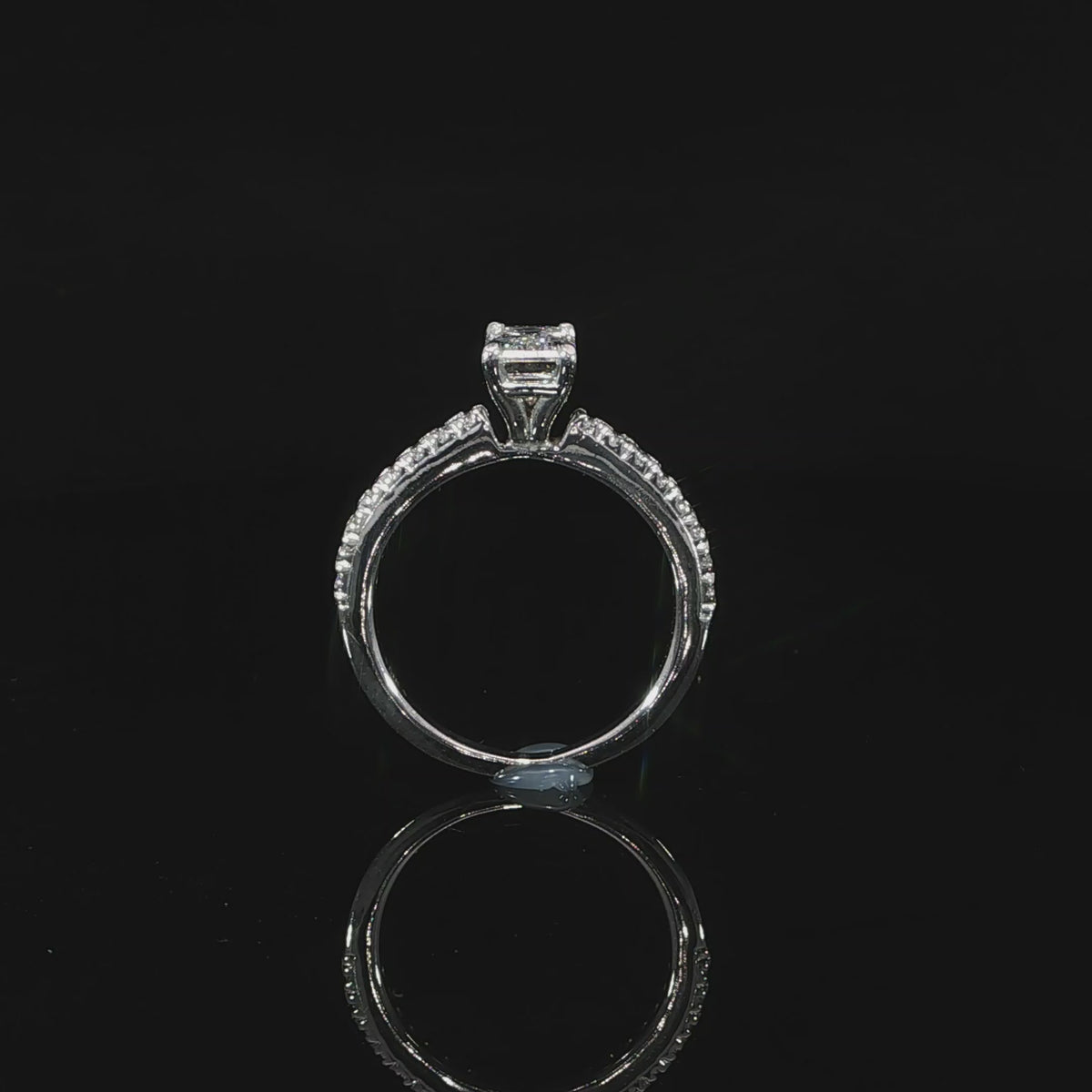 Video of 1 carat emerald-cut diamond held above a slender 14K white gold diamond band.