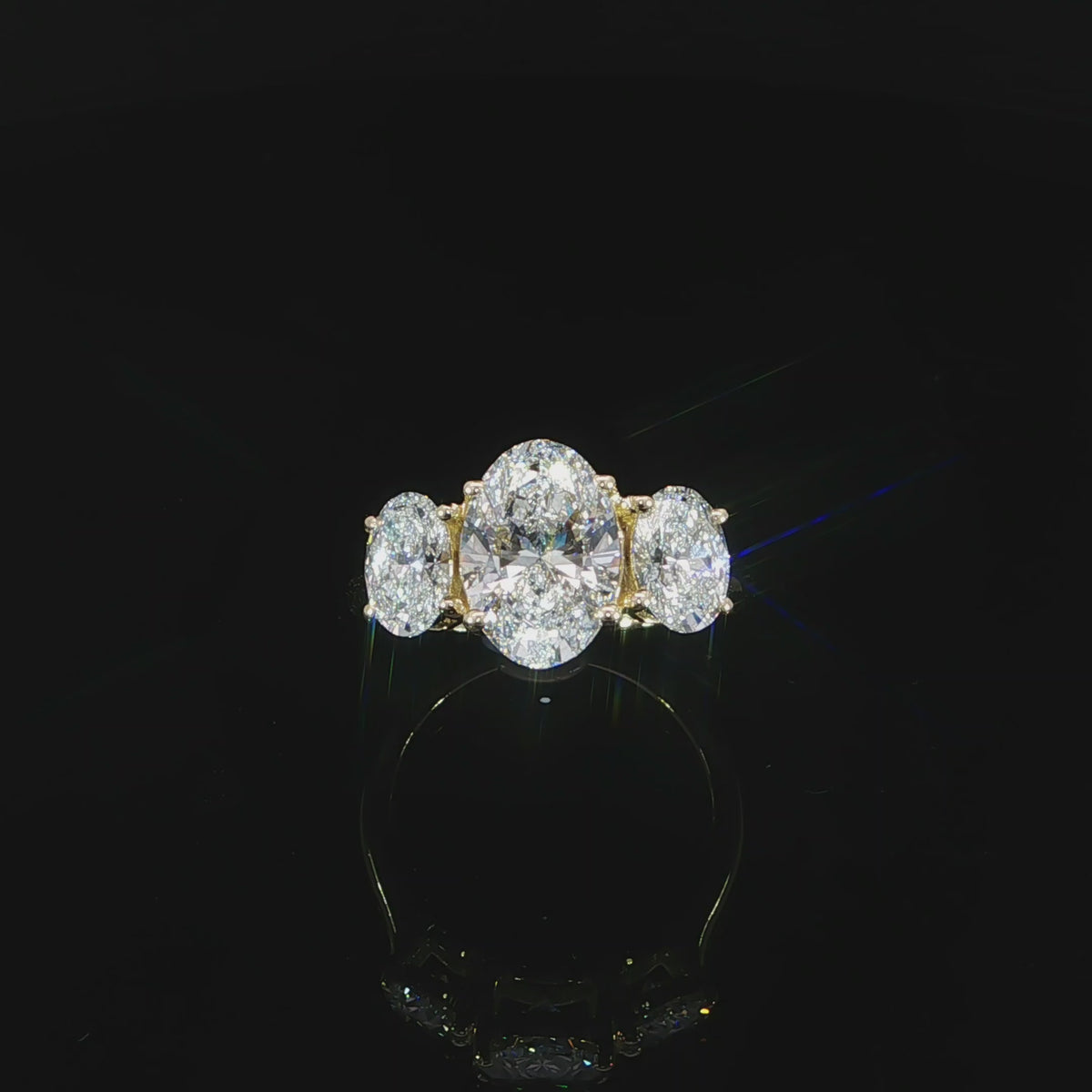 Top video view of a three-stone oval diamond ring with a polished yellow gold band.