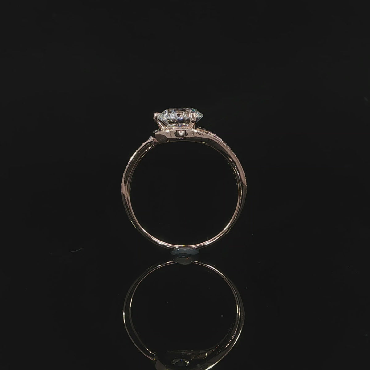 Setting detail of a round brilliant diamond bypass ring with curved diamond-set shoulders in rose gold.