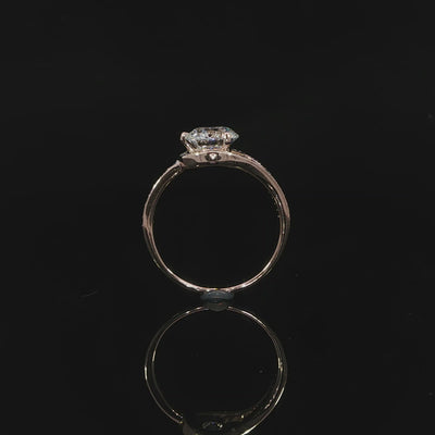 Setting detail of a round brilliant diamond bypass ring with curved diamond-set shoulders in rose gold.