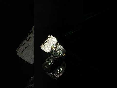 Yellow gold nugget ring resting at an angle on black, with its patterned top and band reflected below.