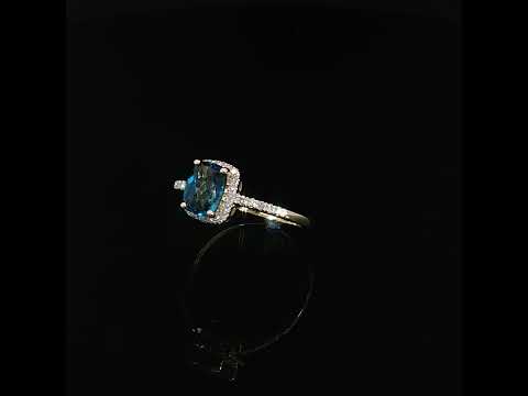 14K yellow gold blue topaz halo ring with 0.09 CTW diamonds, shown at an angle with a reflection.