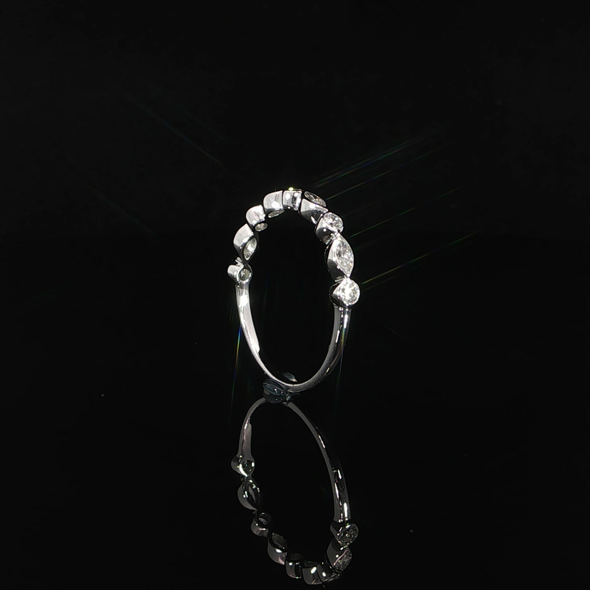 Upright side view of a white gold diamond band showing individual bezel settings and a slim polished shank.
