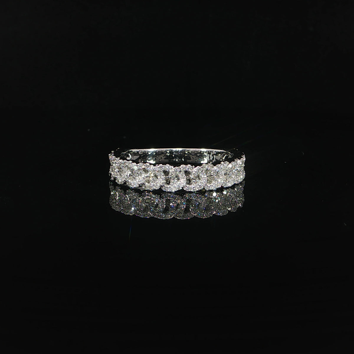 Front view of a white gold diamond band with repeating chain-link motifs on a reflective black surface.