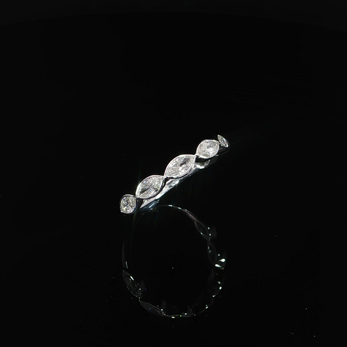 Angled view of a bezel-set marquise lab-grown diamond band on a reflective black surface.