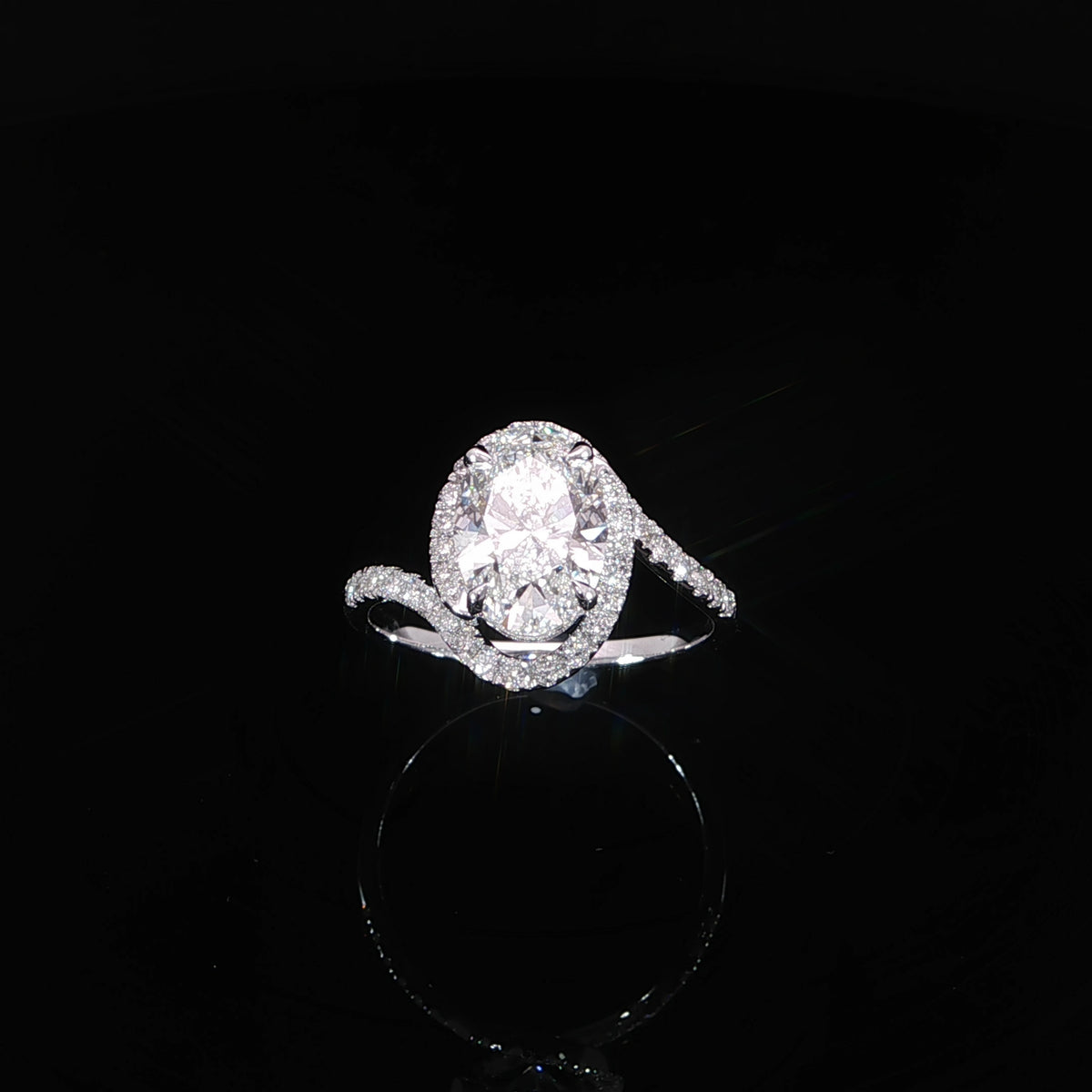 Top view of a white gold oval diamond ring with an asymmetrical bypass band and surrounding halo.
