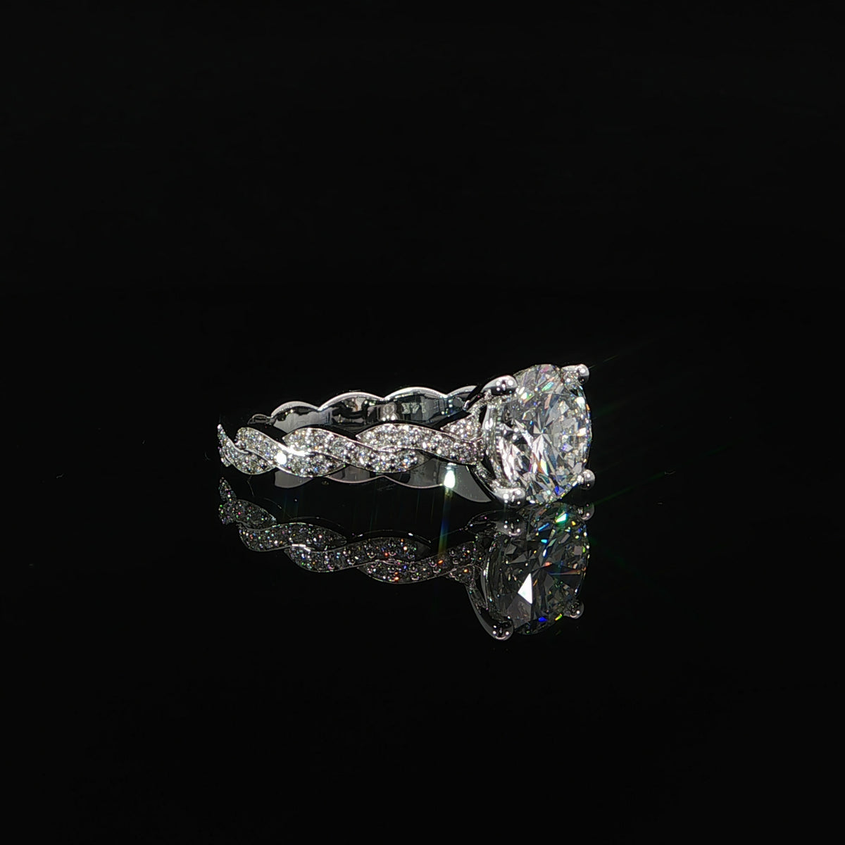 White gold ring resting at an angle, showing the round center diamond and flowing pavé band.