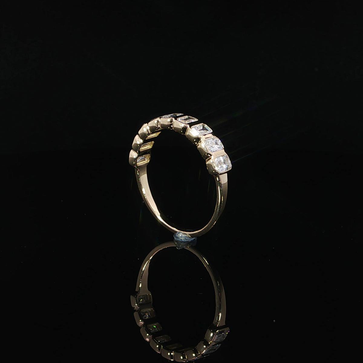 Upright side view of a yellow gold emerald-cut diamond band showing polished bezel walls and a smooth lower shank.