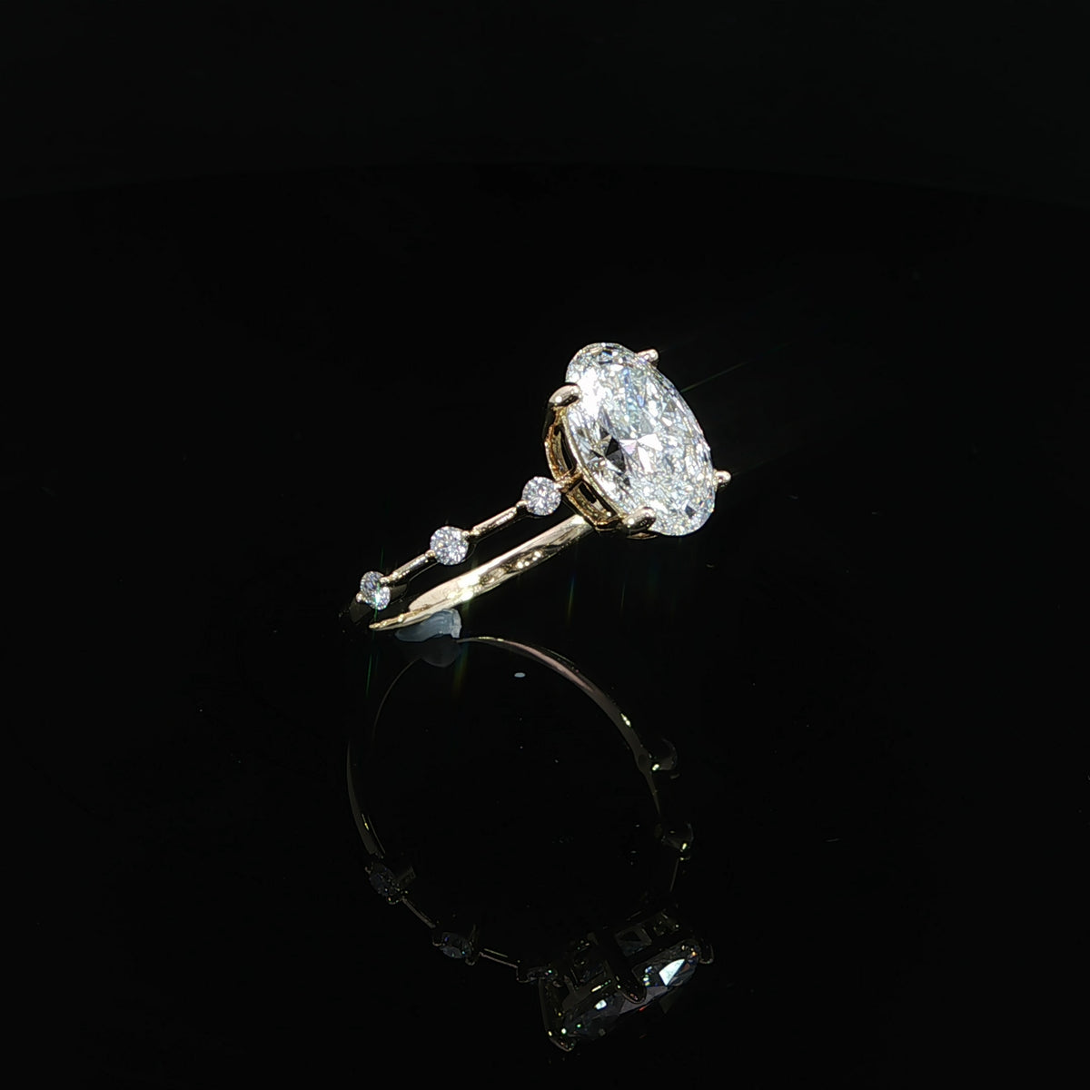 Angled view of an oval diamond engagement ring with a delicate 14K yellow gold station band.